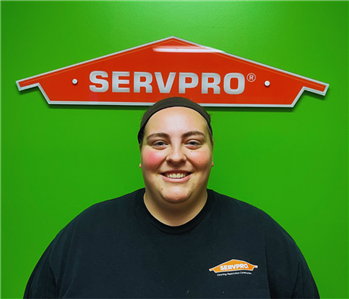employee smiling in front of green wall with orange servpro house