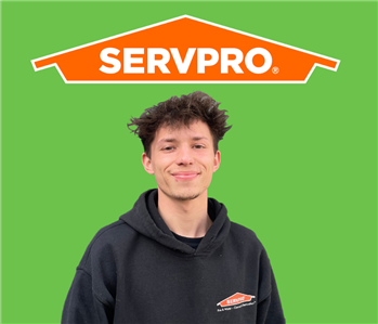 employee smiling in front of green wall with orange servpro house